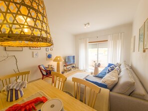 A living room with a sofa, a dining table, chairs, a TV, and a lamp. - Apartment with rooftop terrace - 4 guests (Tavira)