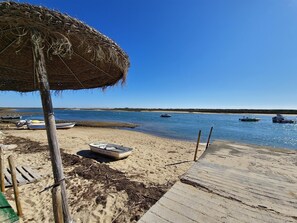 A beach with a wooden deck, a thatched umbrella, and several boats on the water. - Duplex apartment with panoramic view - Unknown number of guests (Tavira)