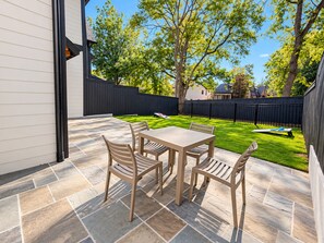 A patio with a table and chairs, a stone floor, a black fence, and a grassy yard. - Luxury 4 Bed 4.5 Bath Townhome-3010 (Homewood)