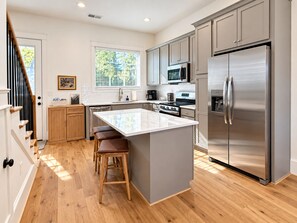 A modern kitchen with a central island, stainless steel appliances, and wooden flooring. - Luxury 4 Bed 4.5 Bath Townhome-3010 (Homewood)