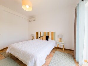 A hotel room with a large bed, a bedside table with lamps, a wall-mounted air conditioner, and a view of the outside. - Villa with private pool and AC - Tavira (Tavira)