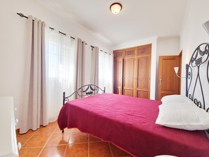 A bedroom with a bed, curtains, a wardrobe, and a door. - T2 Apartment with AC, near beach - 4 guests (Manta Rota)