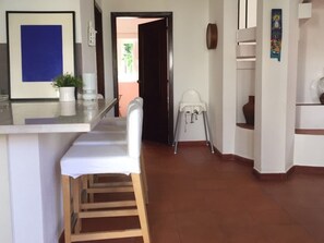 Cozinha com área de bar, cadeira alta e porta que dá para outro cômodo.