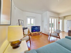 Ein Wohnzimmer mit Fernseher, einer Couch, einer Lampe und einem Couchtisch aus Holz.