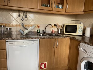 A kitchen with wooden cabinets, a dishwasher, a washing machine, a microwave, and a sink. - Bright apartment near beach - couples/families (Tavira)