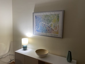 Eine gerahmte Karte von London an einer Wand, ein Nachttisch mit Lampe, Schale und Vase.