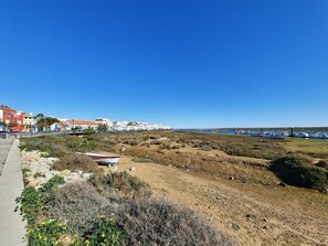 Eine Küstenlandschaft mit einem Feldweg, spärlicher Vegetation und blauem Himmel.