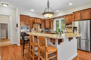 A kitchen with wooden cabinets, a stainless steel refrigerator, a granite countertop, and a chandelier. - Spacious 6-bedroom house in beautiful Fredericksburg with AC (Fredericksburg)