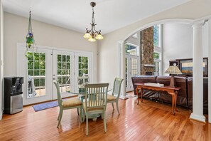 A spacious living room with a wooden floor, a brown leather sofa, a glass coffee table, and a chandelier. - Spacious 6-bedroom house in beautiful Fredericksburg with AC (Fredericksburg)