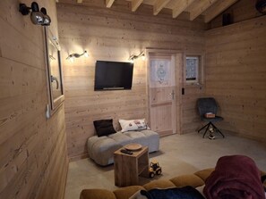 A cozy room with a television mounted on the wall, a wooden door, and a seating area with a sofa and ottoman. - Cozy chalet for 6 in Châtel with WiFi and parking (Châtel)
