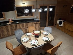 A dining area with a wooden table set for four, surrounded by chairs, and a kitchen area with a counter and cabinets. - Cozy chalet for 6 in Châtel with WiFi and parking (Châtel)