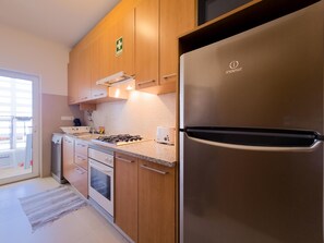 A modern kitchen with stainless steel appliances, wooden cabinets, and a tiled backsplash. - Apartment with pool and garden - 4 guests (Tavira)