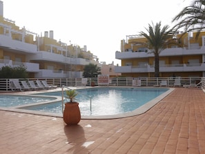 A swimming pool with a tiled deck, surrounded by a white fence, and adjacent to a yellow building with balconies. - Apartment with pool and garden - 4 guests (Tavira)