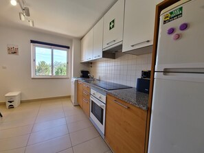 A kitchen with white cabinets, a built-in oven, a refrigerator, and a window with a view of trees. - Spacious apartment with air conditioning - 6 guests (Tavira)