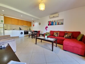 A modern living room with a red sofa, a coffee table, and a dining area with chairs. - Apartment with AC - 2+2 guests (Tavira)