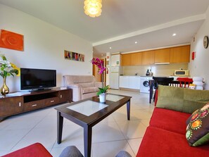 A modern living room with a flat-screen TV, sofa, coffee table, and a kitchen area with a washing machine and microwave. - Apartment with AC - 2+2 guests (Tavira)