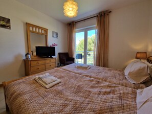 A hotel room with two beds, a television on a dresser, a chair, and a balcony with curtains. - Apartment with AC - 2+2 guests (Tavira)