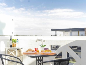 A terrace with a table set for breakfast, including croissants and orange juice, overlooking a modern building and a clear sky. - Studio with AC, WiFi - 2 adults, 1 child (Tavira)