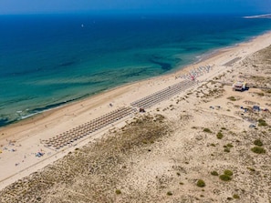 An aerial view of a beach with rows of sun loungers and umbrellas, a sandy shore, and the ocean in the background. - Studio with AC, WiFi - 2 adults, 1 child (Tavira)