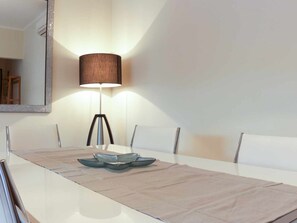 A dining table with a reflective surface, surrounded by chairs, and a floor lamp with a cylindrical shade. - 2-bedroom apartment near Tavira (Tavira)