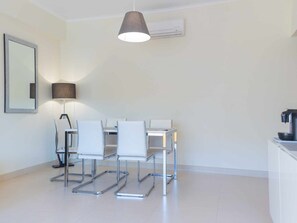 A modern, minimalist room with a dining table and chairs, a lamp, and an air conditioning unit. - 2-bedroom apartment near Tavira (Tavira)