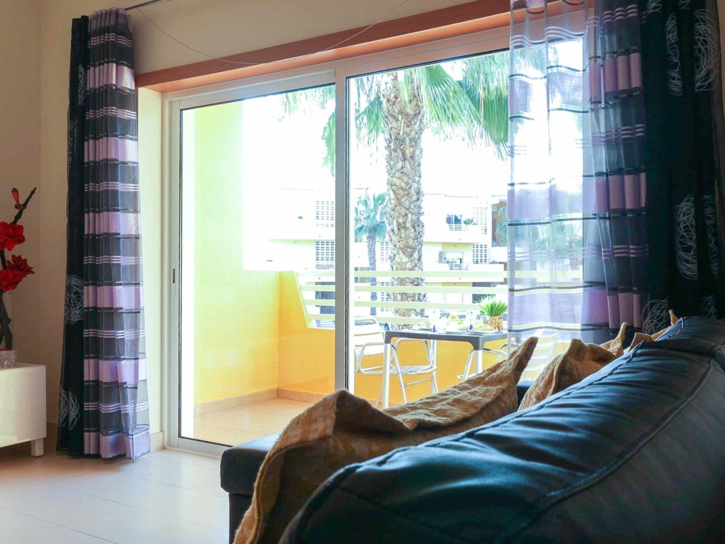 A room with a sofa, a table with chairs, and a view through a sliding glass door to an outdoor balcony.