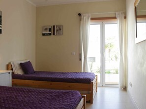 A bedroom with two beds, a window with curtains, and a door leading to an outdoor area. - Stylish apartment with air conditioning - 4 guests (Tavira)