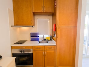 A compact kitchen with wooden cabinets, a stainless steel sink, and a built-in oven. - Studio with AC, Wi-Fi and pool - 2+1 guests (Tavira)