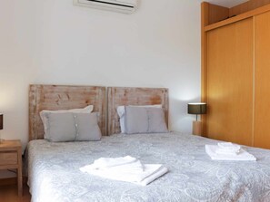 A double bed with a patterned bedspread, two pillows, a wooden headboard, a nightstand with a lamp, and a wooden door. - Apartment with air conditioning - 6 guests (Tavira)