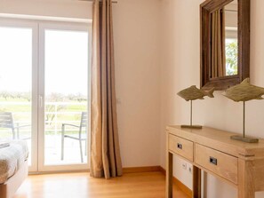 A room with a sliding glass door leading to an outdoor area, a wooden desk with drawers, and a mirror on the wall. - Apartment with air conditioning - 6 guests (Tavira)