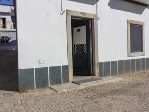 A building with a white facade, a black door with a metal grid, and a small window with a metal grid. - Charming apartment in historic centre - 3 guests (Tavira)