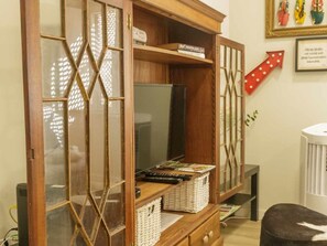 A room with a wooden cabinet with glass doors, a television, and a red arrow decoration on the wall. - Charming apartment in historic centre - 3 guests (Tavira)
