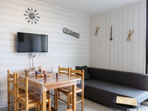 A dining area with a wooden table and chairs, a television mounted on the wall, and a sofa. - Charming studio mountain view - 4 guests (Saint-Lary-Soulan)