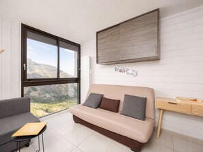 A modern living room with a sofa, a small table, and a large window offering a mountain view. - Charming studio mountain view - 4 guests (Saint-Lary-Soulan)