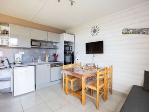 A compact kitchen with a dining area, a flat-screen TV mounted on the wall, and a clock decoration. - Charming studio mountain view - 4 guests (Saint-Lary-Soulan)