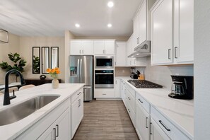 A modern kitchen with white cabinetry, stainless steel appliances, and a wooden floor. - New 5BR Reunion Villa, Themed Rooms, Resort Pools (Kissimmee)
