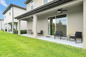 A residential building with a covered patio area featuring outdoor seating and a ceiling fan. - New 5BR Reunion Villa, Themed Rooms, Resort Pools (Kissimmee)
