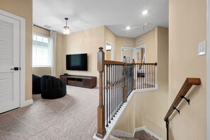 A home interior with a staircase, a flat-screen TV, a bean bag, and a wooden entertainment unit. - New 5BR Reunion Villa, Themed Rooms, Resort Pools (Kissimmee)