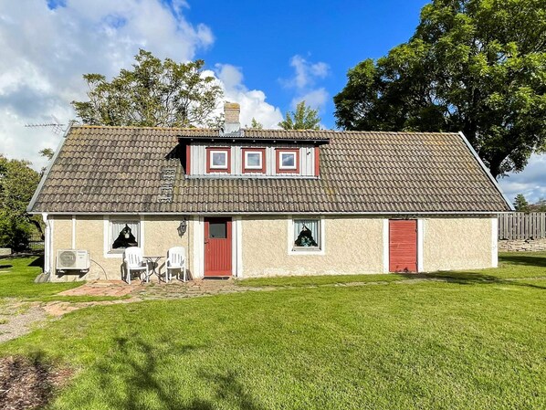 A single-story house with a tiled roof, a red door, and a small porch with two chairs. - 4 Person Holiday Home in Kopingsvik (Kopingsvik)