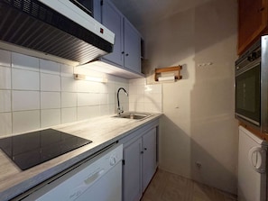 A compact kitchen with white tiles, a built-in dishwasher, a stainless steel sink, and a microwave. - Cozy studio with forest view - 4 guests (Les Orres)