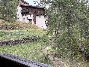 A multi-story building with balconies, surrounded by trees and a stone wall. - Cozy studio with forest view - 4 guests (Les Orres)