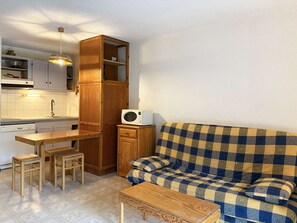 A compact living space with a kitchenette, wooden furniture, and a checkered sofa. - Cozy studio with forest view - 4 guests (Les Orres)