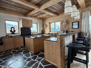 A kitchen with wooden cabinets, a central island, and a stone-patterned floor. - Refined chalet at Mont-Blanc - 15 guests (Saint-Gervais-les-Bains)