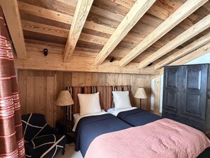 Ein Zimmer mit Holzboden, einem Bett, zwei Lampen, einem Kleiderschrank und einem Vorhang.