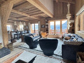 A spacious living area with a high ceiling, wooden beams, a sofa set, a dining area, and a view of mountains through large windows. - Refined chalet at Mont-Blanc - 15 guests (Saint-Gervais-les-Bains)