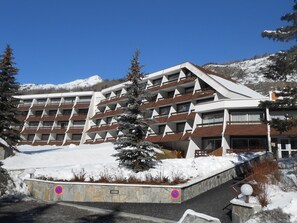 A multi-story hotel with a modern architectural design, featuring balconies and a snow-covered landscape in the background. - Cozy studio - 4 guests (Saint-Chaffrey)