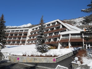 A multi-story hotel with a modern architectural design, featuring balconies and a snow-covered landscape in the background. - Cozy studio, south-facing balcony - 4 guests (Saint-Chaffrey)