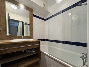 Casa de banho com toucador de madeira, espelho, lavatório branco e banheira com azulejos azuis.