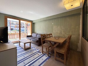 A furnished room with a sofa, dining table, chairs, a television, and a view through a sliding glass door. - Renovated apartment in Les Orres - 6 guests (Les Orres)
