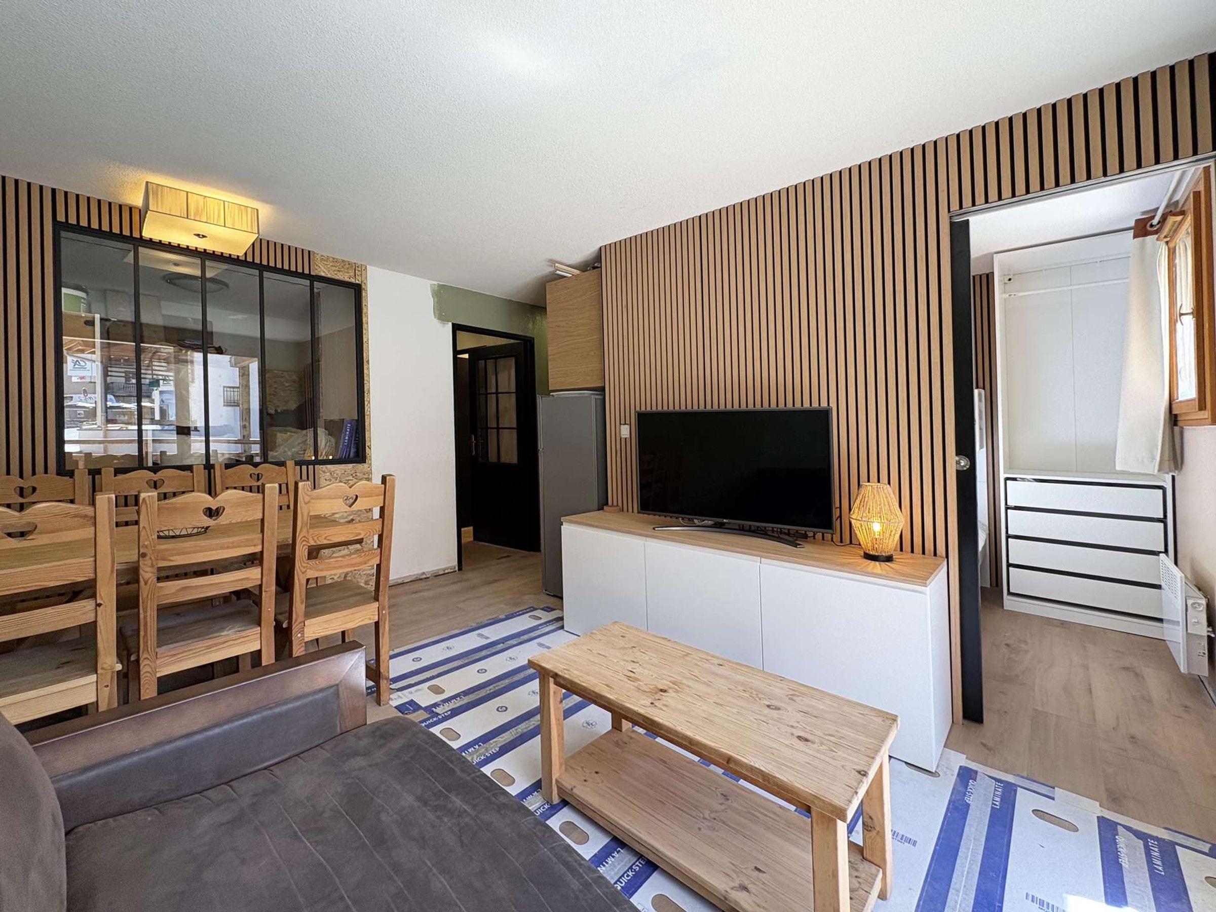 A modern living room with a flat-screen TV, wooden furniture, and a patterned floor.